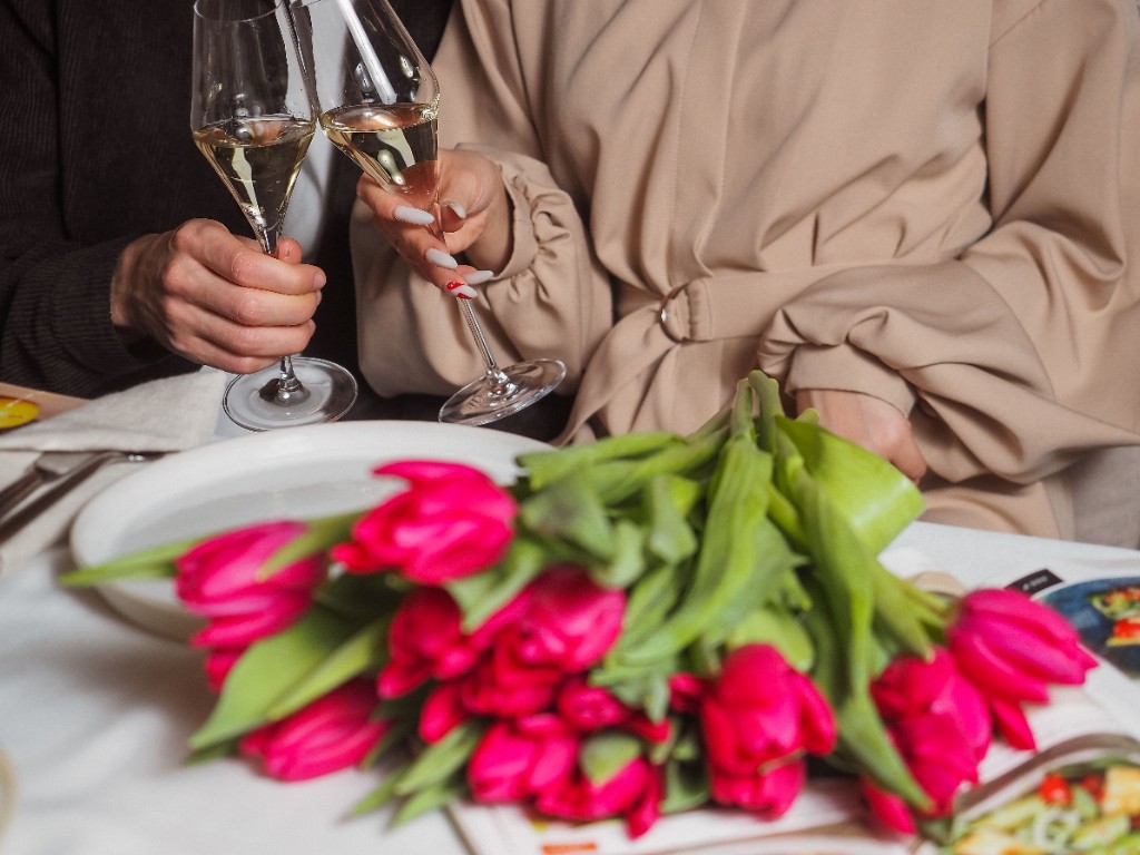 A couple toasting with champagne glasses beside a bouquet of pink tulips