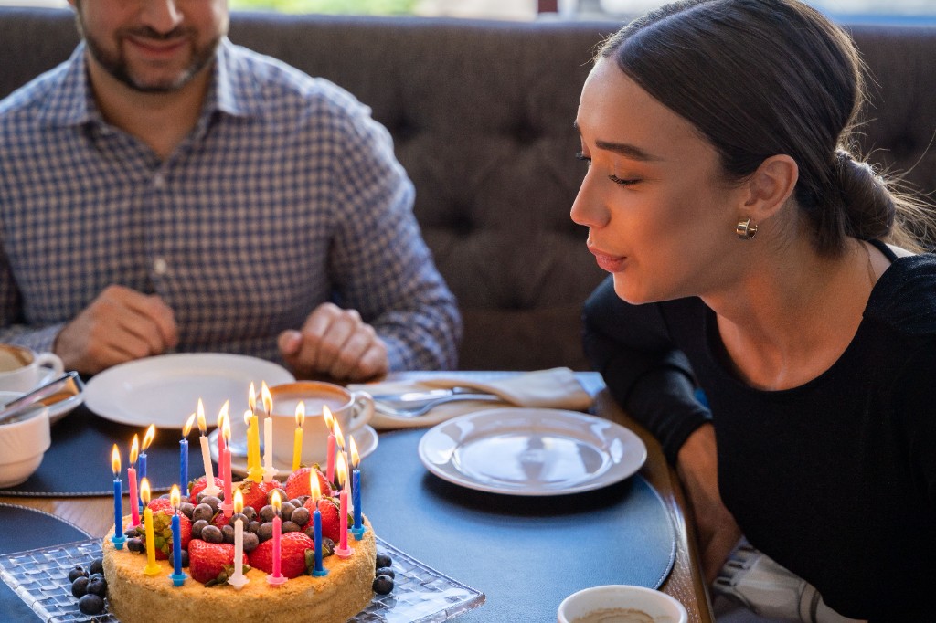 A woman blowing out candles on a strawberry birthday cake