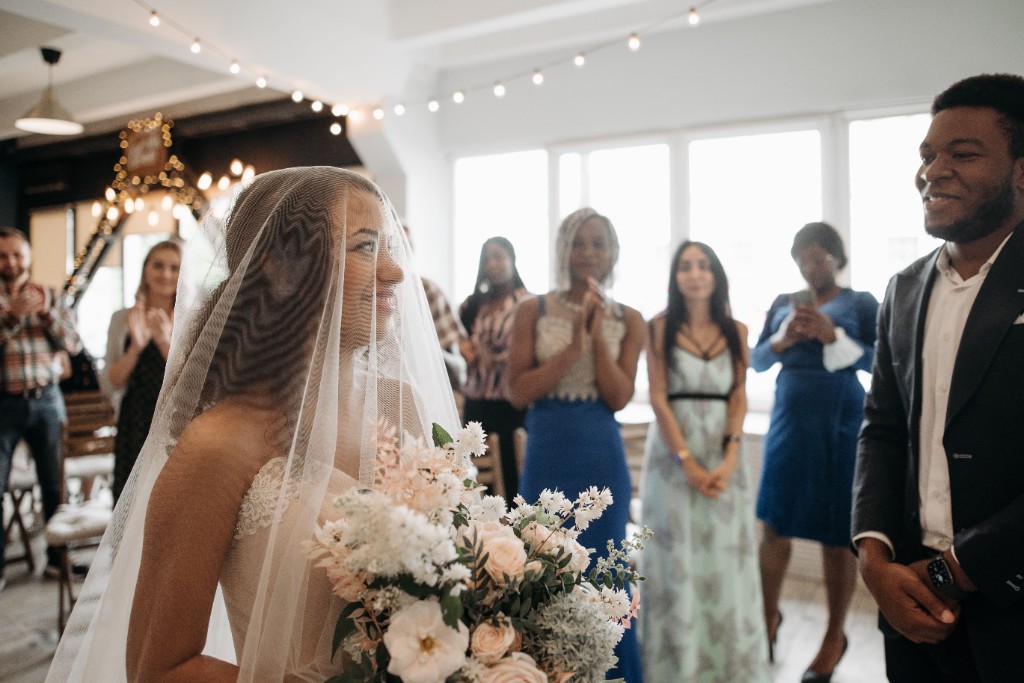 A bride in a veil holding a bouquet facing the groom during a wedding ceremony